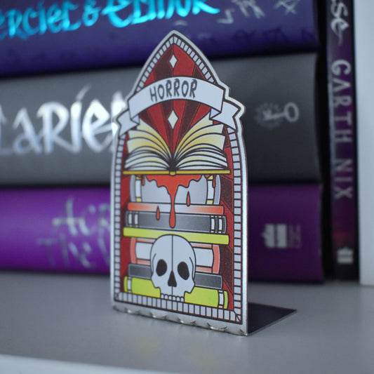 Decorative stainless steel standee with 'Horror' design on in the style of a stained glass window at an angle to see it is an L shape with a stack of books behind.