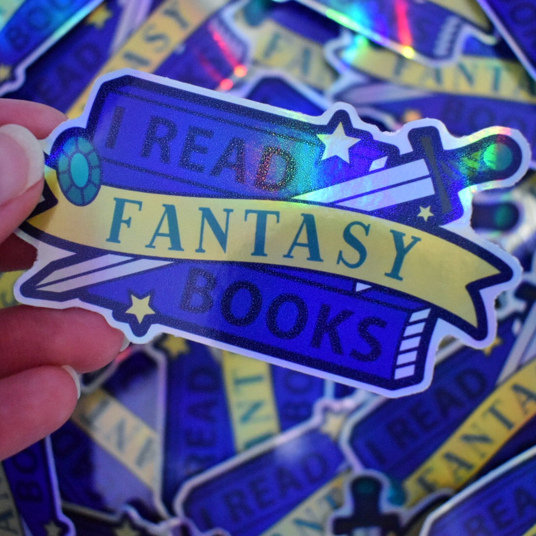 White hand holding sticker, tilted at an angle to show the holographic effect. Sticker design is a stack of dark blue books with a grey bladed sword, with a brown and blue hilt/handle. A blue gem and stars are scattered on the design. A yellow banner across the middle of the design. The design reads I read fantasy books. Sticker has a white border all around the design. Background is blurry/distance of the same stickers scattered.