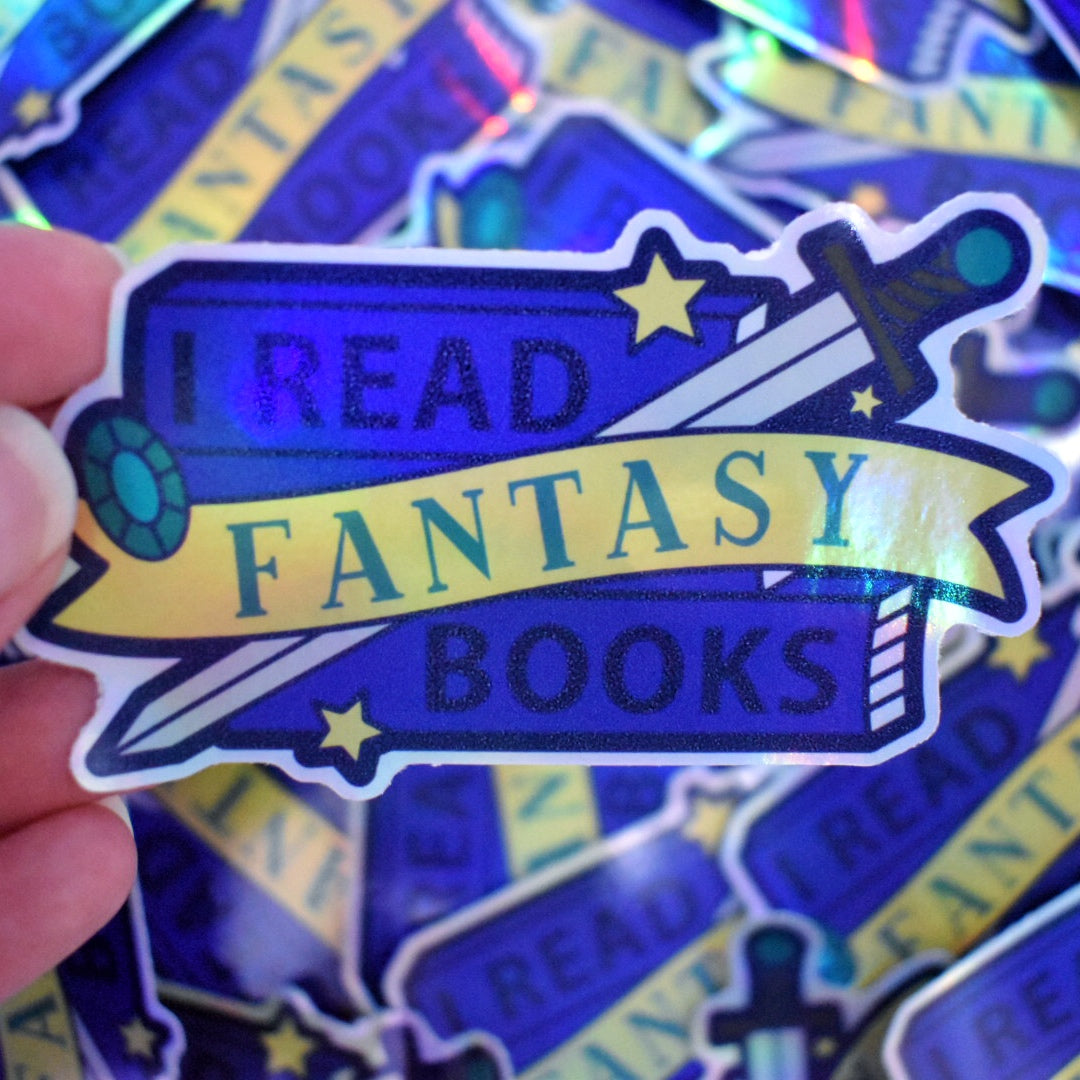 White hand holding sticker. Sticker design is a stack of dark blue books with a grey bladed sword, with a brown and blue hilt/handle. A blue gem and stars are scattered on the design. A yellow banner across the middle of the design. The design reads I read fantasy books. Sticker has a white border all around the design. Background is blurry/distance of the same stickers scattered.