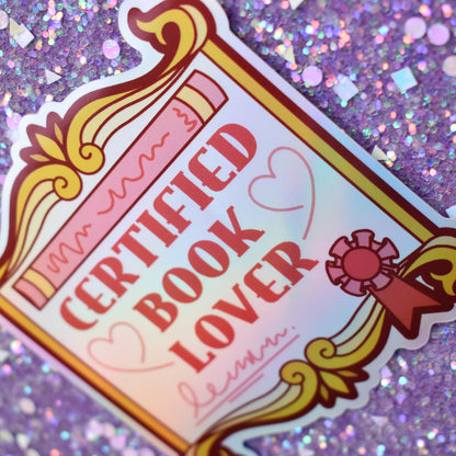 Bookish holographic sticker with 'Certified Book Lover' text, designed to look like an award/fancy scroll, on a glittery purple background