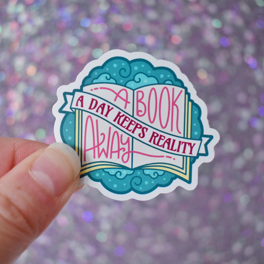 Bookish mini sticker with 'A book a day keeps reality away' text on top of a open book & teal cloud design, held by a white hand against a glittery purple background