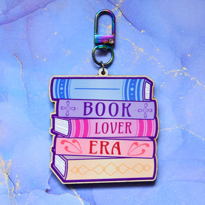 Wooden keyring with colourful book stack design with detailed spines and 'Book Lover Era' text. On a colourful watercolour style background.