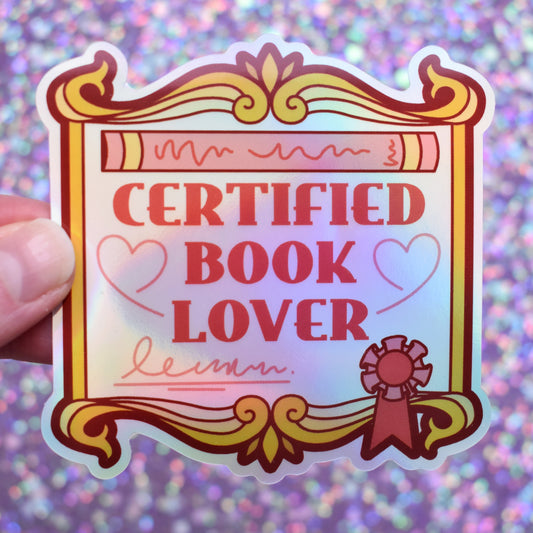 Bookish holographic sticker with 'Certified Book Lover' text, designed to look like an award/fancy scroll, held by a white hand against a glittery purple background