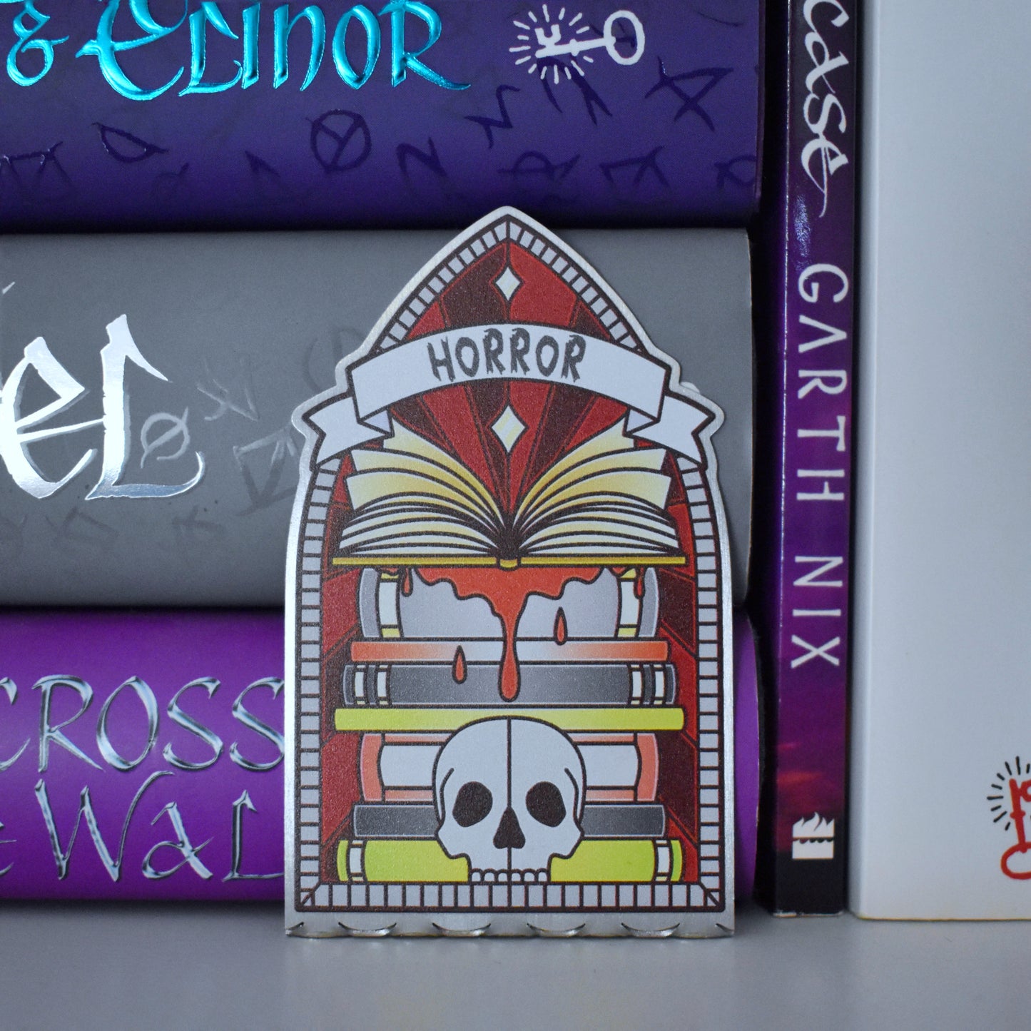Decorative stainless steel standee with 'Horror' design on in the style of a stained glass window pushed up against a stack of books.