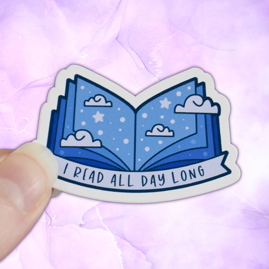 Bookish mini sticker with 'I read all day long' text on a banner, on top of open blue pages book with scattered clouds & stars/dots, held by a white hand against a pastel purple background