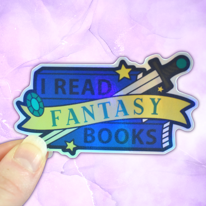 Bookish holographic sticker with 'I read fantasy books' text on a banner, on top of a stack of blue books with a sword, gem and star details, held by a white hand against a pastel purple background
