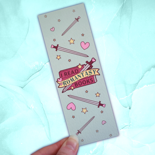 Textured bookmark with 'I Read Romantasy Books' text on a small stack of books and banner, with a sword illustration, in the centre of the design. Smaller swords, hearts and stars fill the rest of the bookmark space. Held by a white hand against pastel teal background.