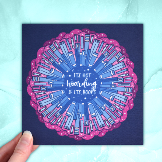Square bookish print featuring a repeating pattern of blue bookspines and pink cloud/swirls with darker blue around the edge. Design reads 'it's not hoarding if it's books' in white/light blue at the centre of the design. Held by a white hand against background of pastel teal.