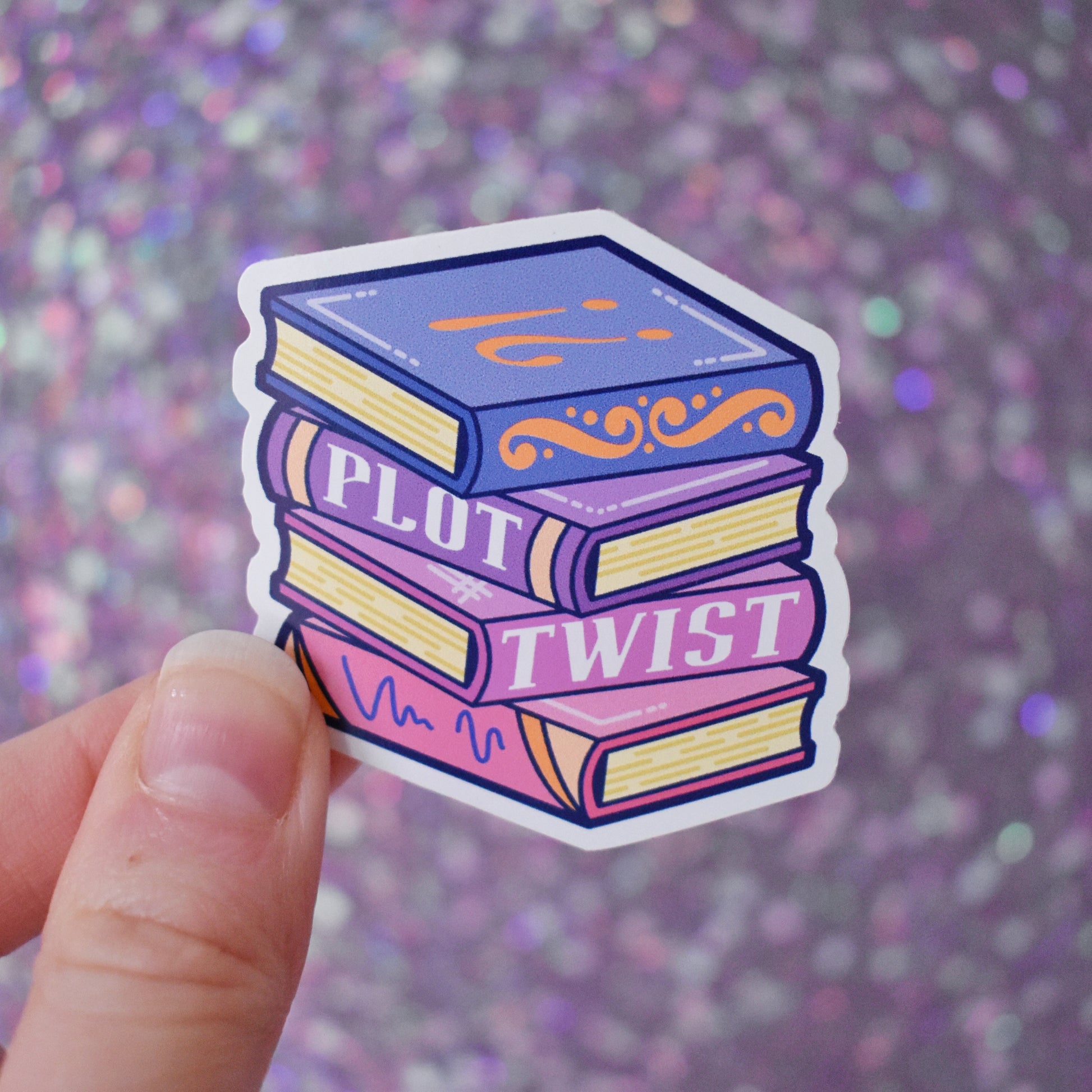 Bookish mini sticker of a stack of books in blues, purples and pinks with 'Plot Twist' text. Held by a white hand on a purple glittery background.