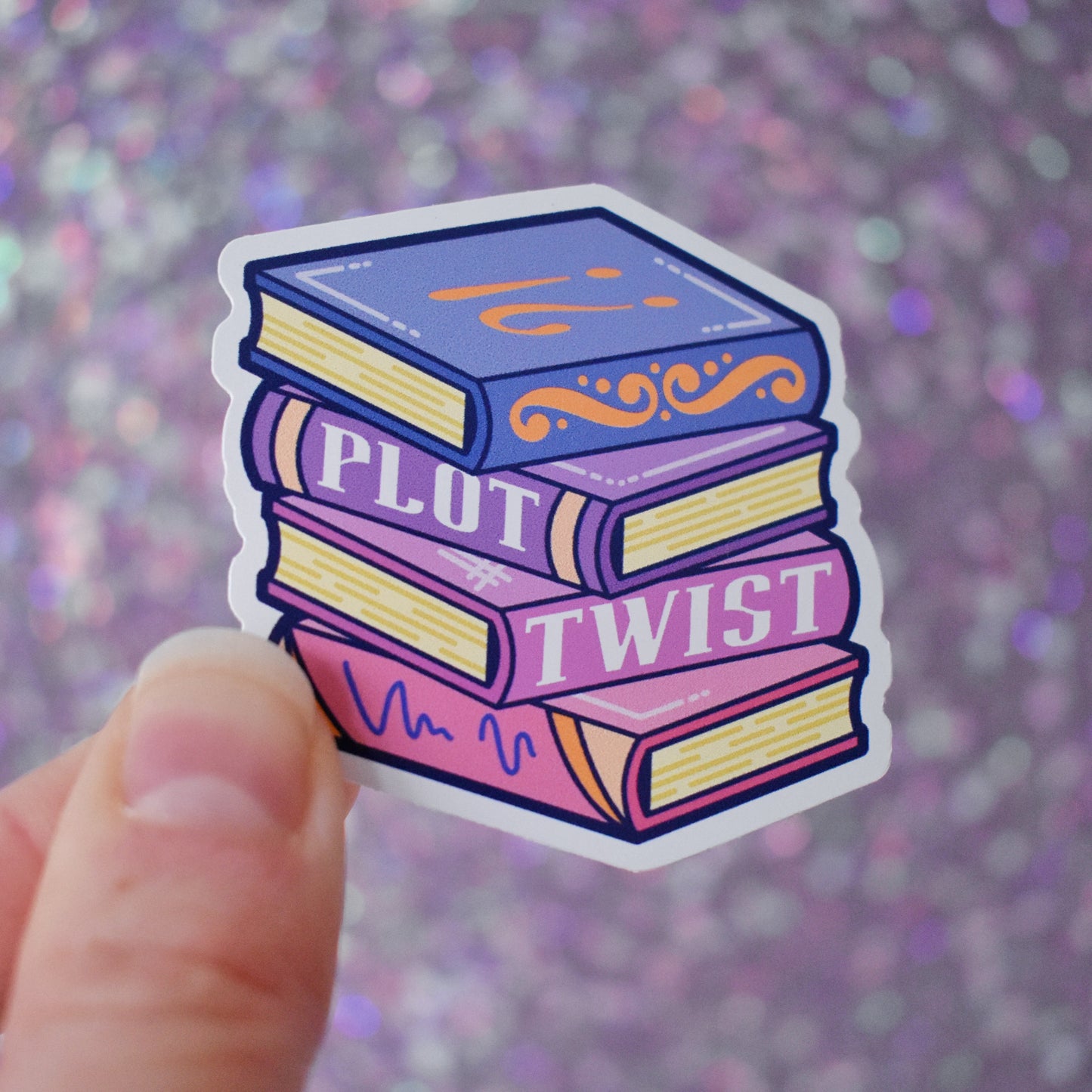 Bookish mini sticker of a stack of books in blues, purples and pinks with 'Plot Twist' text. Held by a white hand on a purple glittery background.