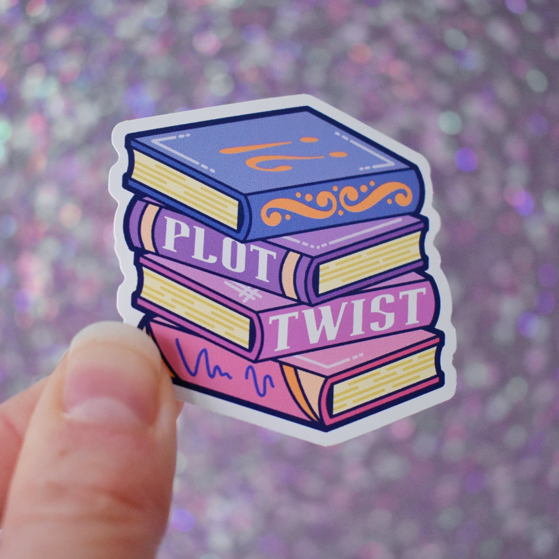 Bookish mini sticker of a stack of books in blues, purples and pinks with 'Plot Twist' text. Held by a white hand on a purple glittery background.