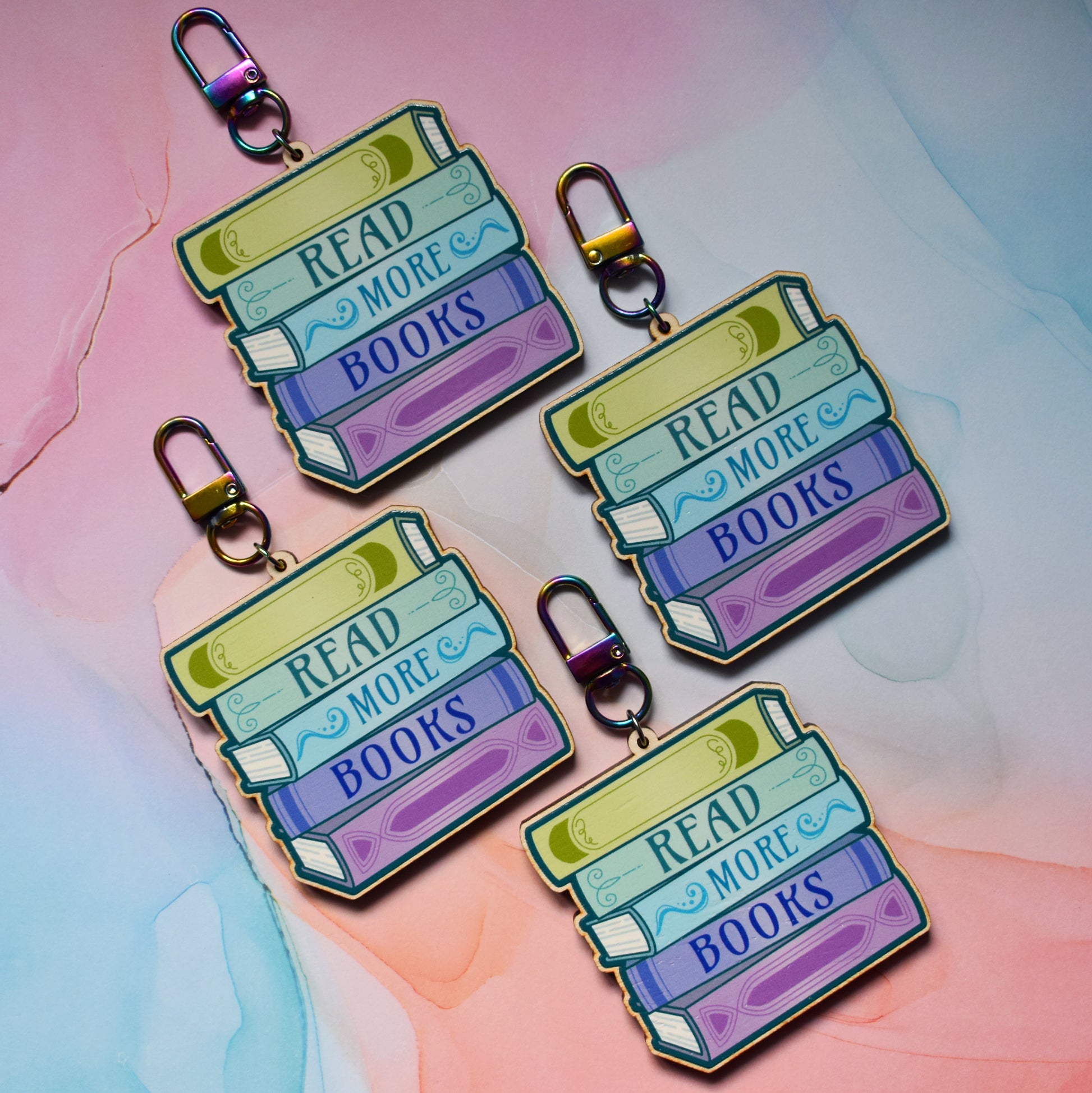 Four wooden keyrings in a slanted diamond shape, with a colourful book stack design with detailed spines and 'Read More Books' text. On a colourful watercolour style background.