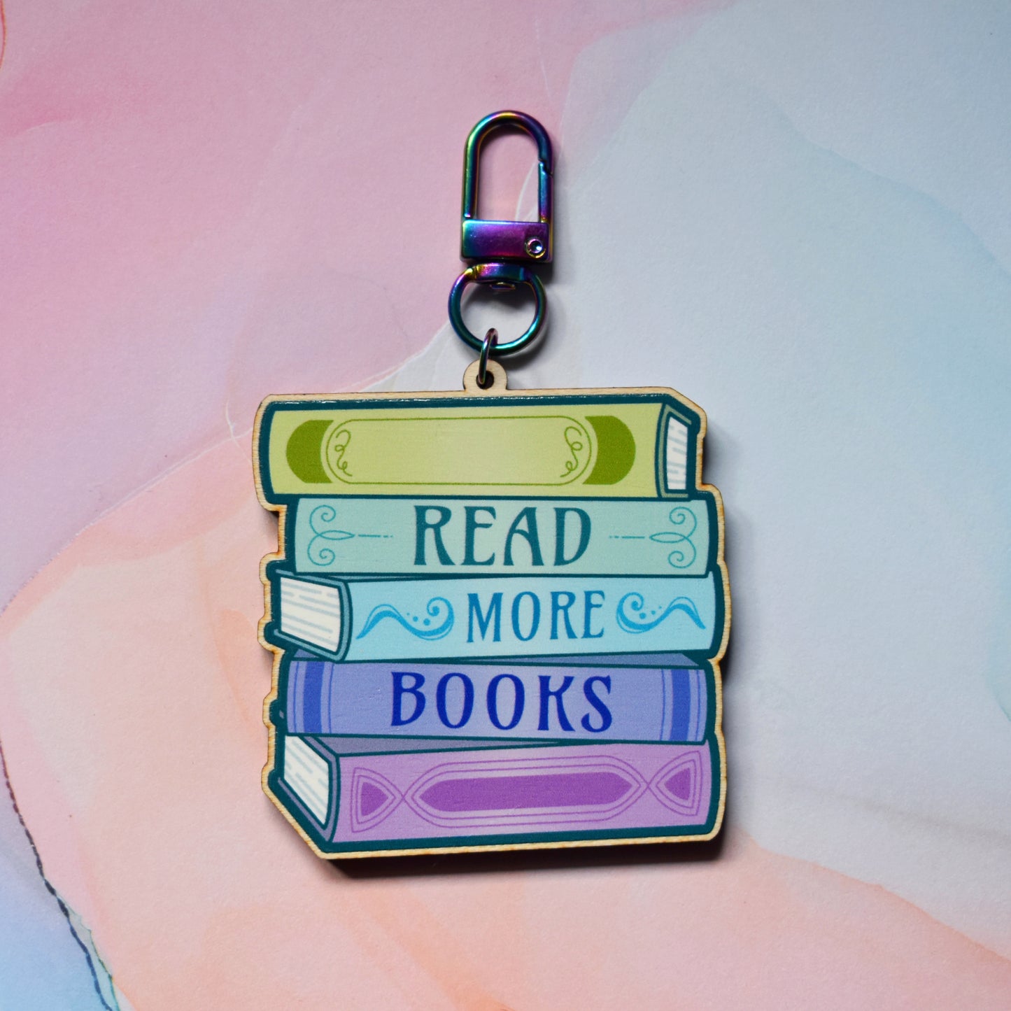 Wooden keyring with colourful book stack design with detailed spines and 'Read More Books' text. On a colourful watercolour style background.
