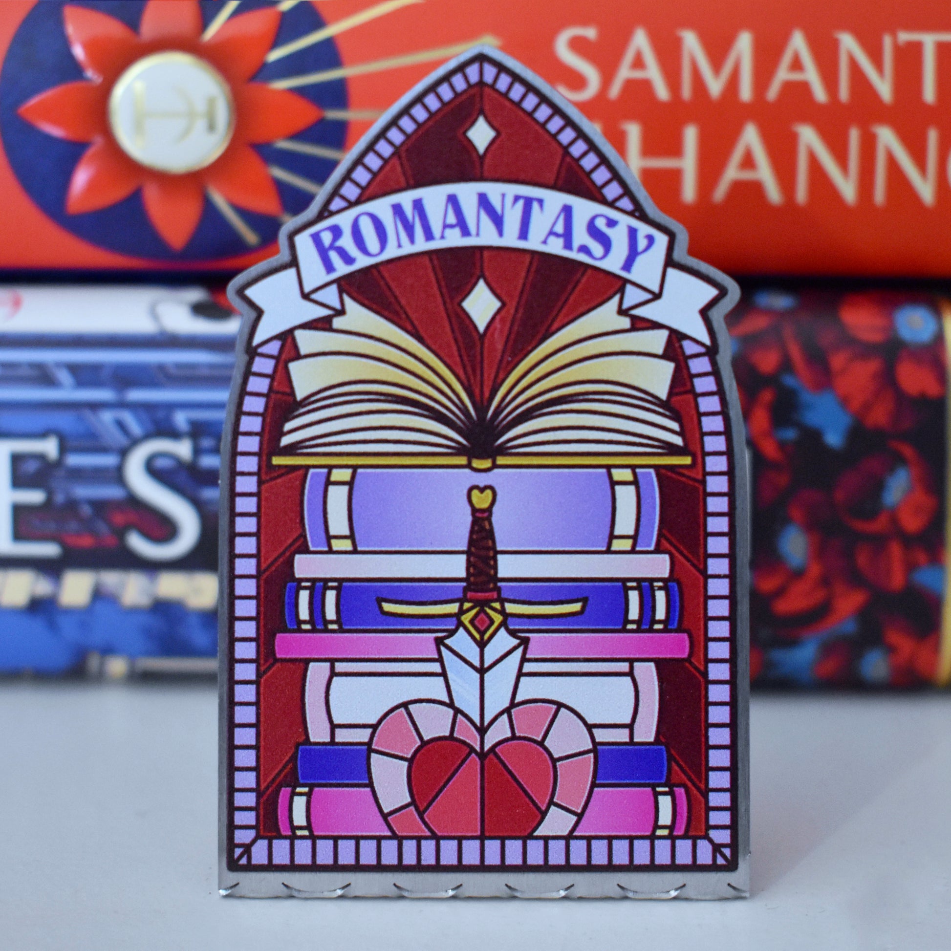 Decorative stainless steel standee with 'Romantasy' design on in the style of a stained glass window with a stack of books behind.