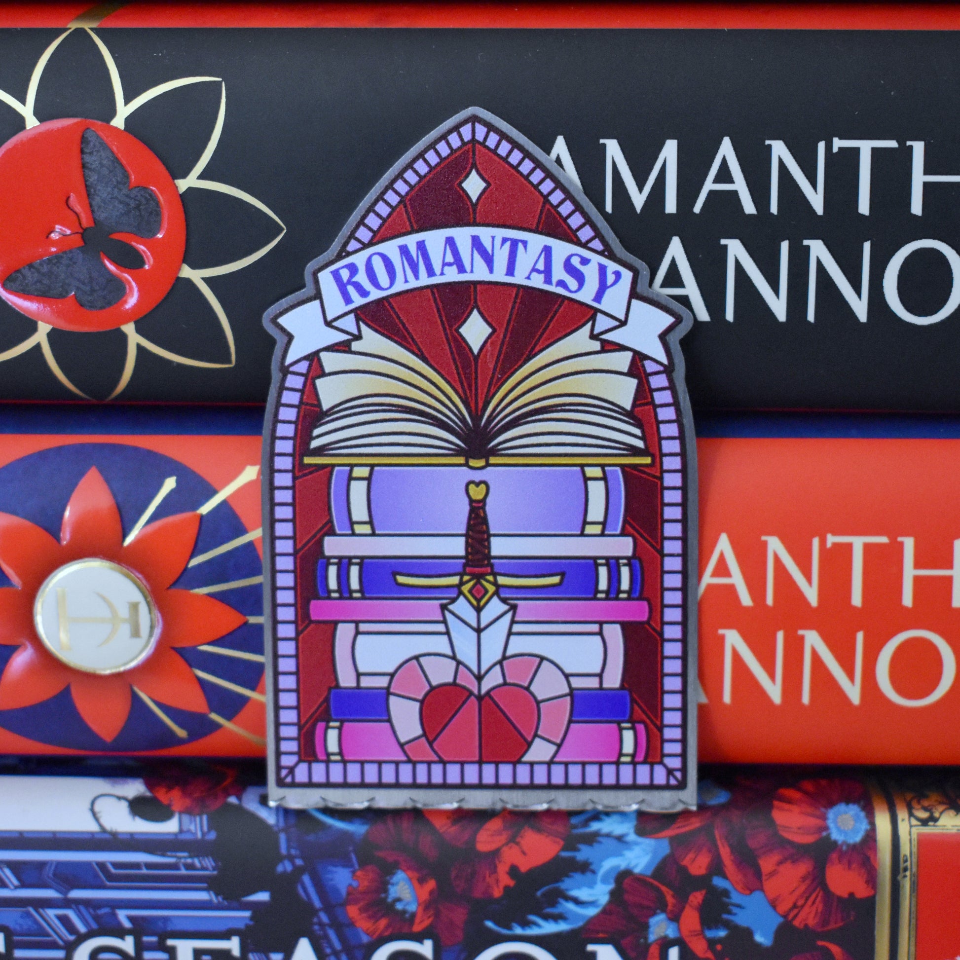 Decorative stainless steel standee with 'Romantasy' design on in the style of a stained glass window pushed between a stack of books.