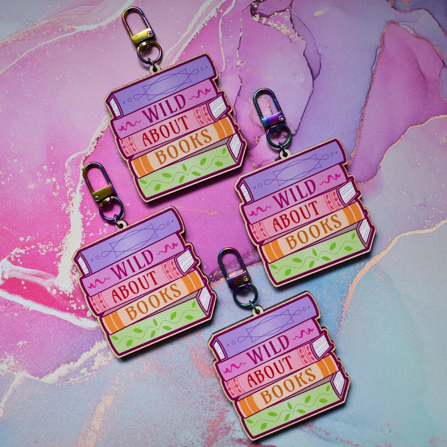 Four wooden keyrings in a slanted diamond shape, with a colourful book stack design with detailed spines and 'Wild About Books' text. On a colourful watercolour style background.