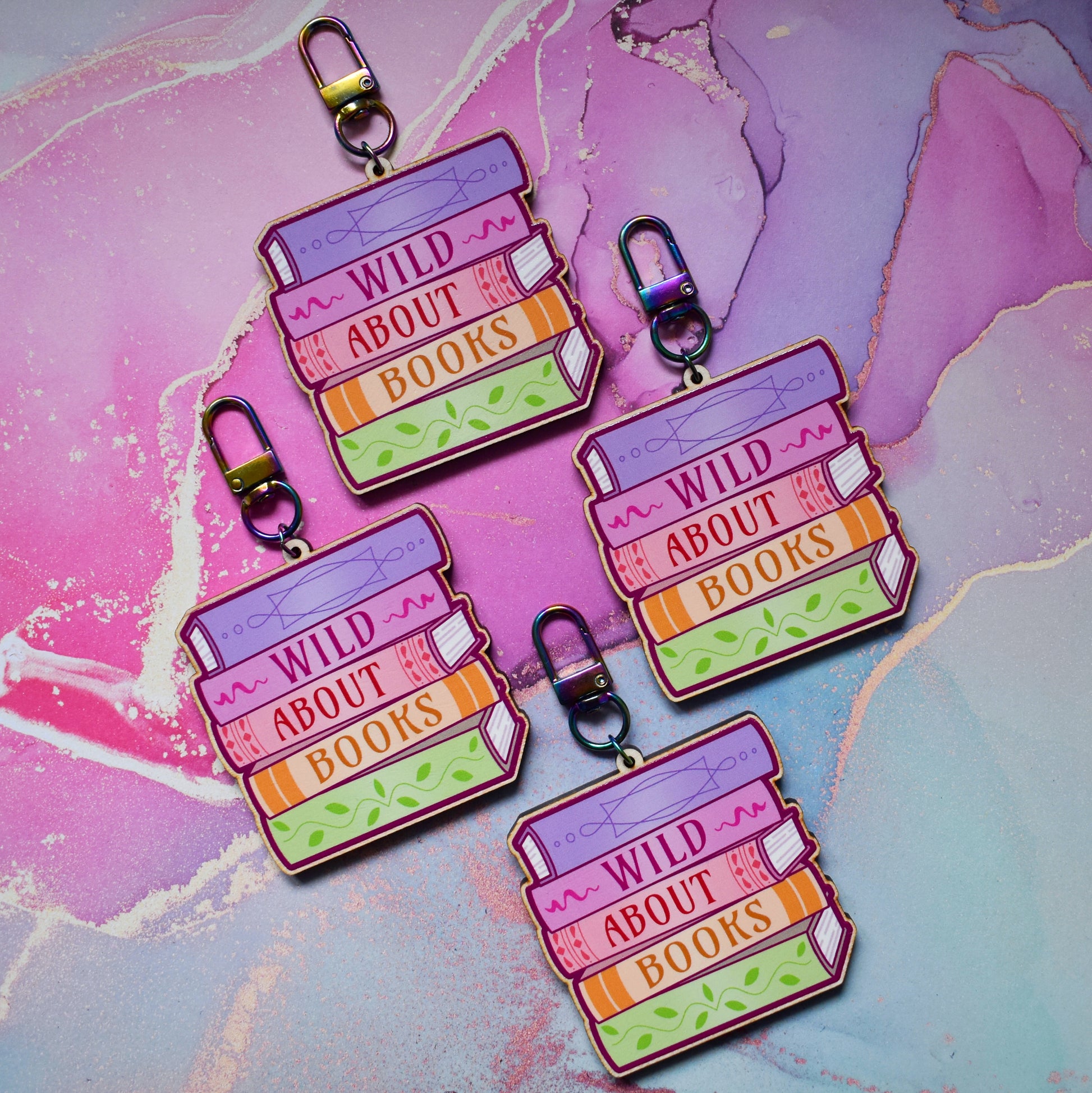 Four wooden keyrings in a slanted diamond shape, with a colourful book stack design with detailed spines and 'Wild About Books' text. On a colourful watercolour style background.