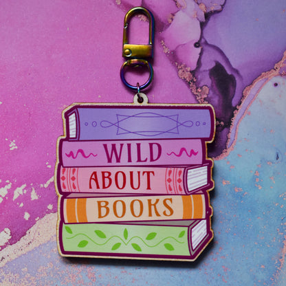 Wooden keyring with colourful book stack design with detailed spines and 'Wild About Books' text. On a colourful watercolour style background.