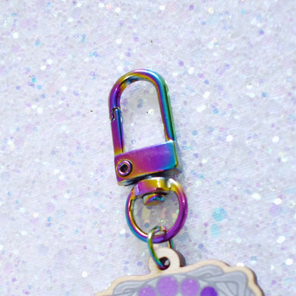 Close up of rainbow metal keychain attachment with lopster style clasp, attached to the top of wooden charm.